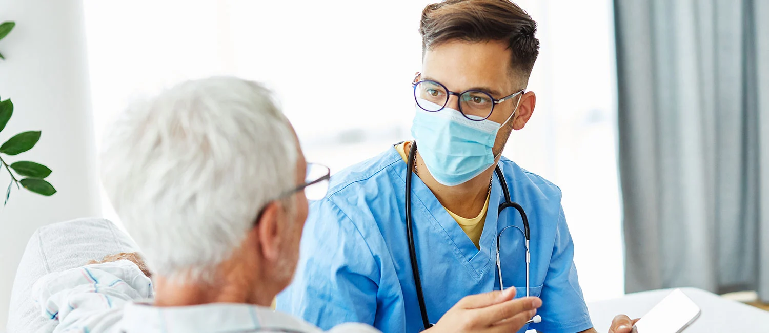 A Vista Springs clinician in scrubs sitting bedside with a Member during a care visit